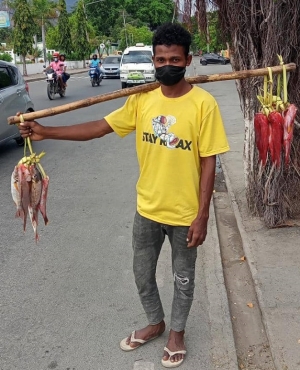 Negosiante ikan, Julio Correia, faan hela ikan iha estrada ninin area Largo Lesidere nia oin. Foto:Bernadino/INDEPENDENTE.